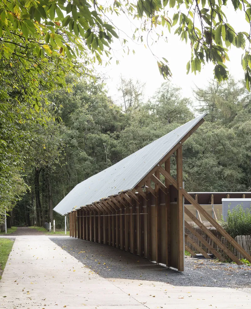 Long view of the slanted roof pavilion with exposed timber columns and overhanging branches