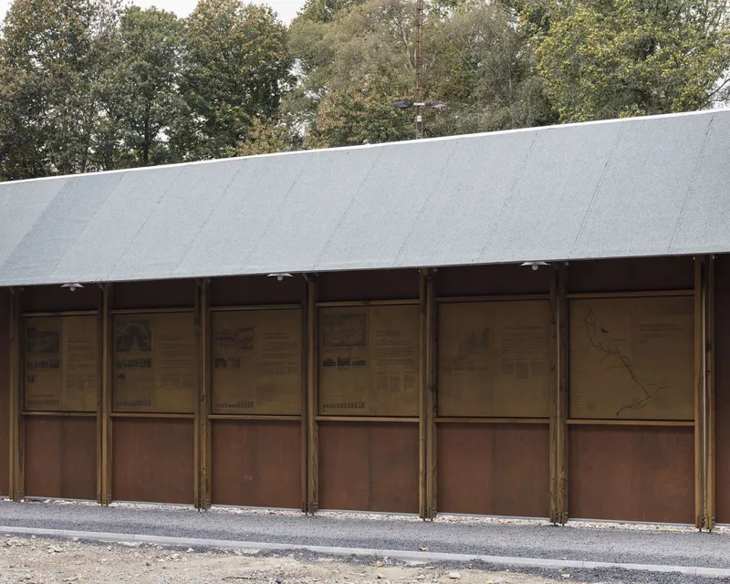 Exterior wall of vertical timber framing with corten-clad lower panels beneath a sloping metal roof