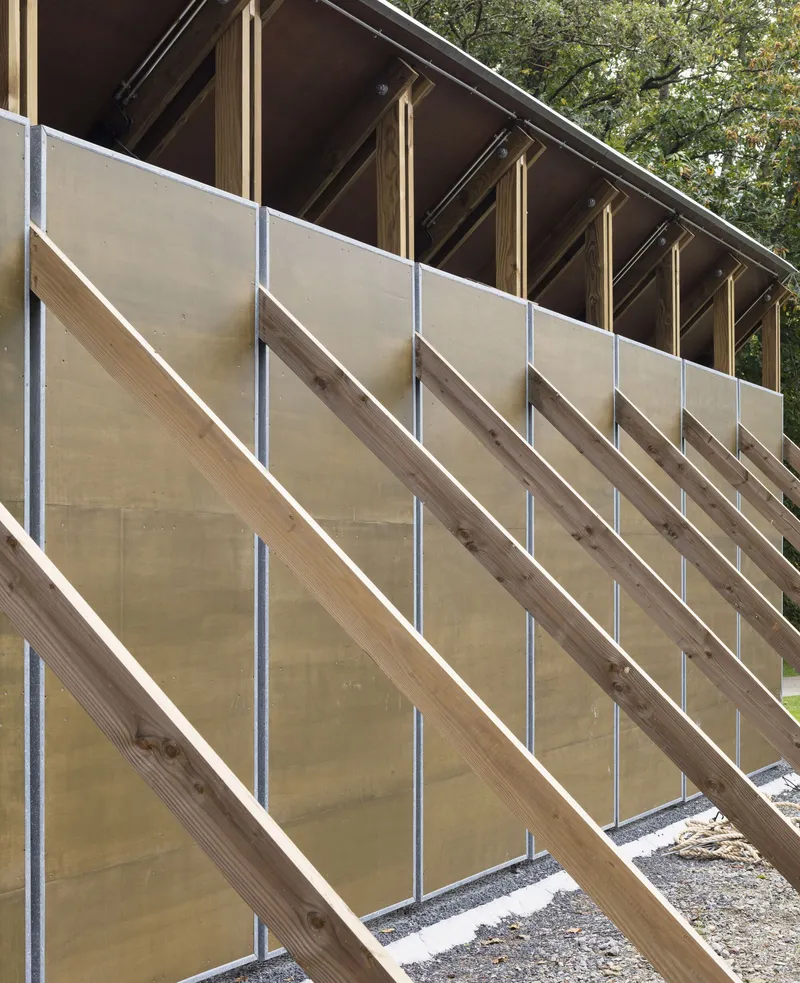 Diagonal timber bracing with metal tension rods supporting plywood wall panels under exposed rafters