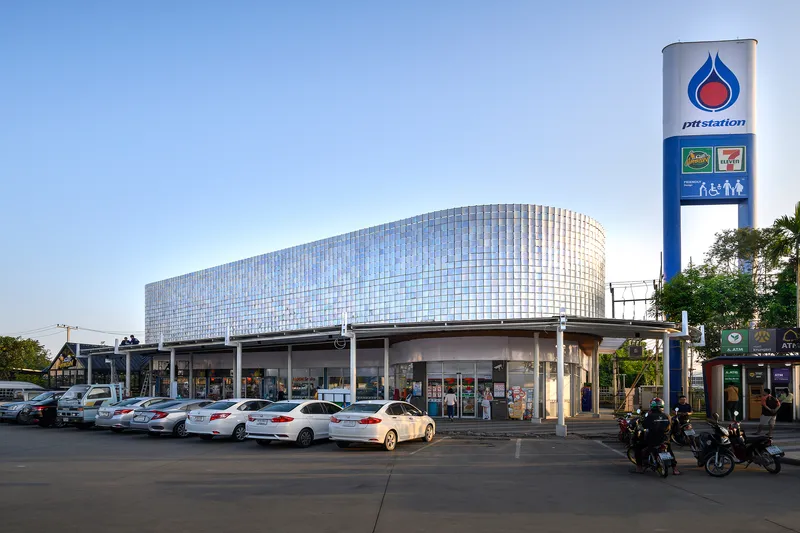 Curved facade with vertical glass panel cladding atop a ground-level service station under a clear sky
