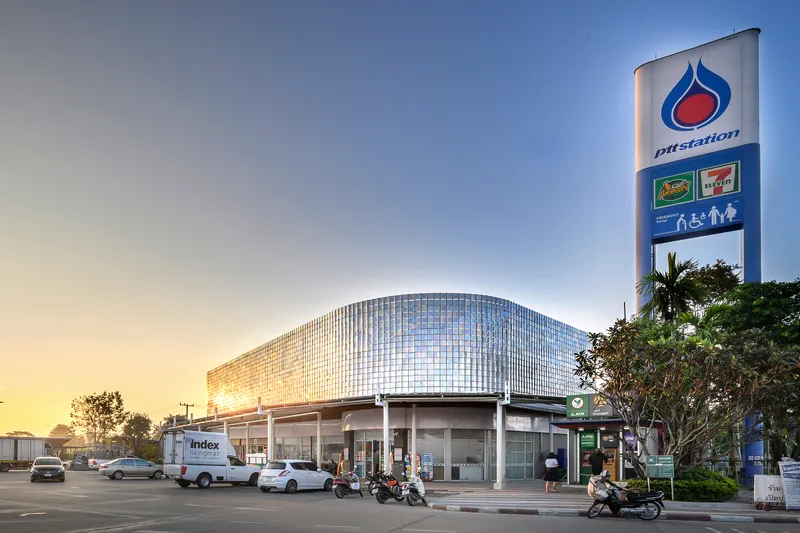 Rounded translucent glass panel facade above a canopy with vehicles and motorcycles at dusk