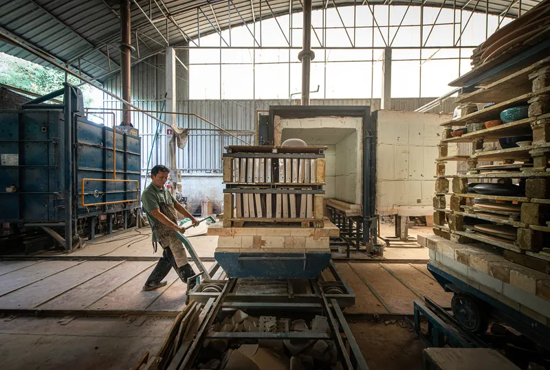 Worker loading ceramic pieces into the brick kiln within the industrial workshop space