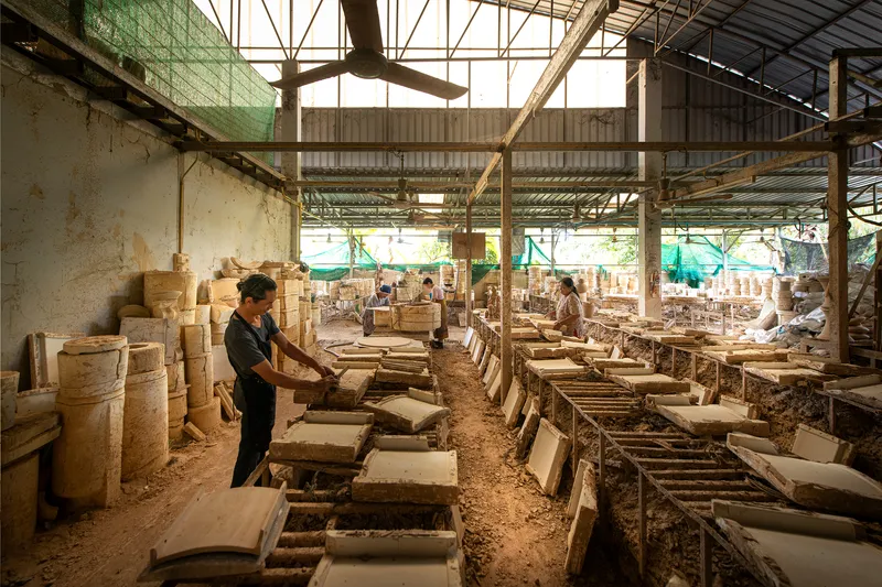 Interior of ceramics workshop with workers forming clay pieces under the skylit steel truss roof