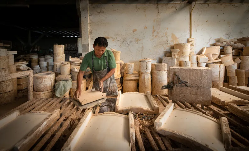 Craftsman inspecting unfired ceramic tiles arranged on wooden drying racks in a tile workshop