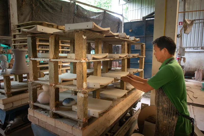 Craftsman loading unfired ceramic tiles into a multi-tiered wooden kiln rack
