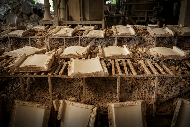 Close-up of stacked ceramic tile molds covered in drying clay and sediment within a workshop interior