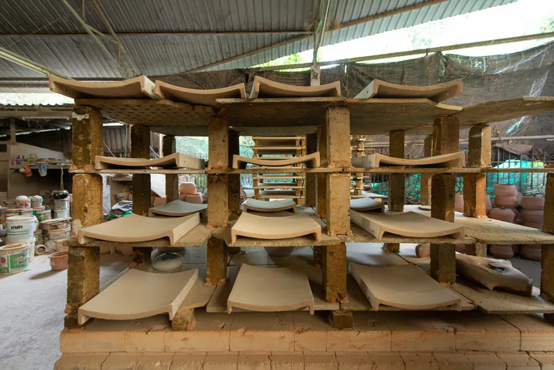 Multi-tiered drying rack with curved ceramic tiles resting on timber shelves under corrugated metal roofing