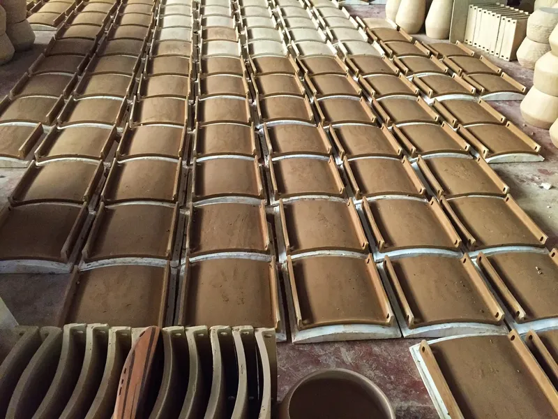 Top-down view of curved ceramic roof tiles arranged in rows on a workshop floor