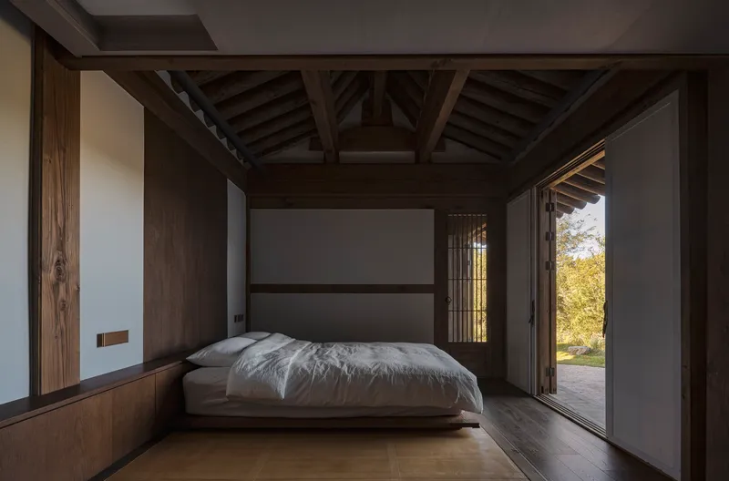 Bedroom with exposed timber structure and sliding doors opening to the exterior garden