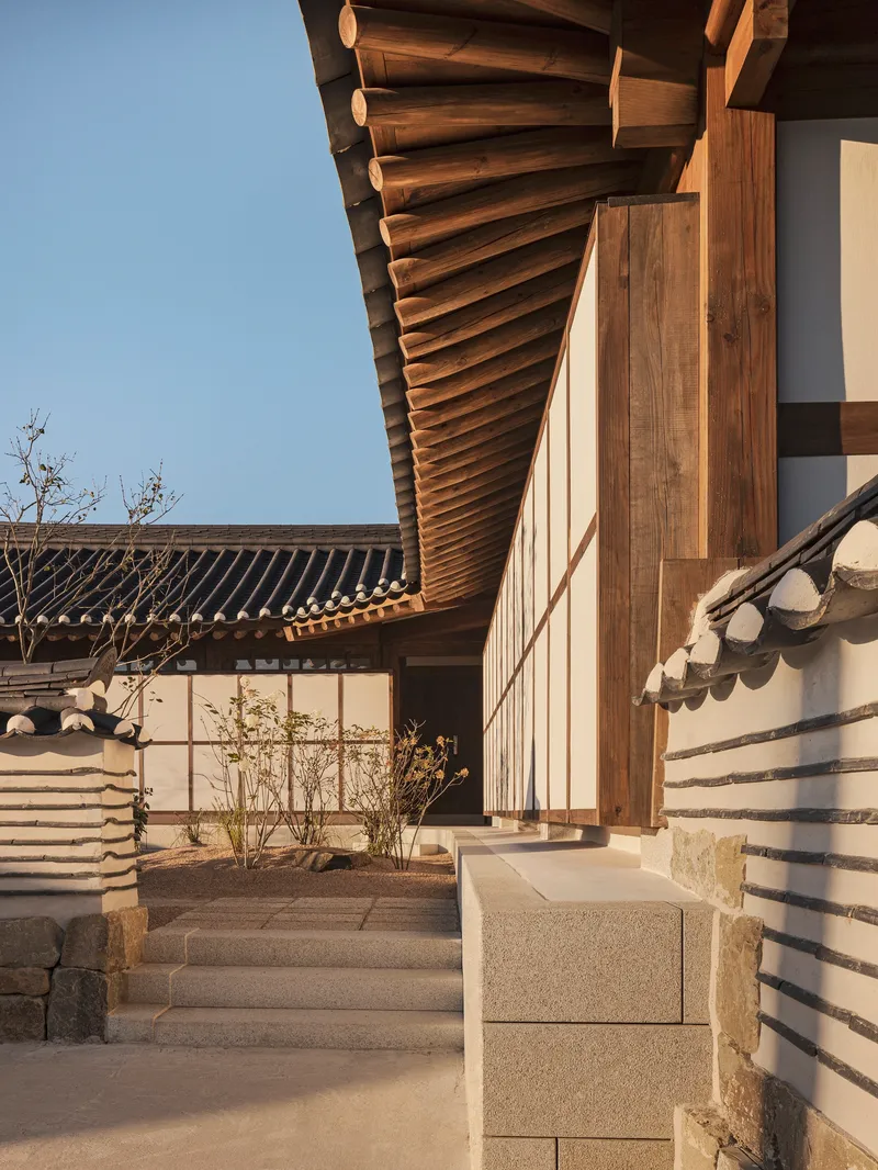 Stone steps leading into a courtyard with exposed timber rafters and planted beds at golden hour