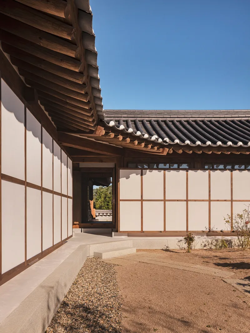 Courtyard passage with translucent screen walls and gravel garden under curved tile roof eaves