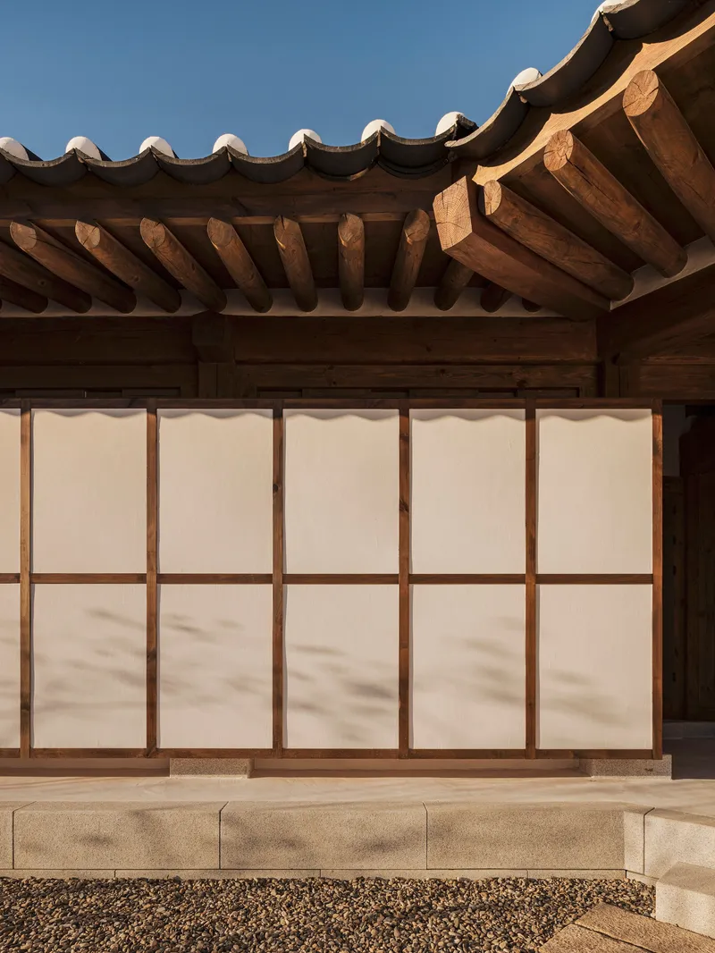Exterior wall with translucent paper panels in timber frames below a tiled eave with exposed rafters