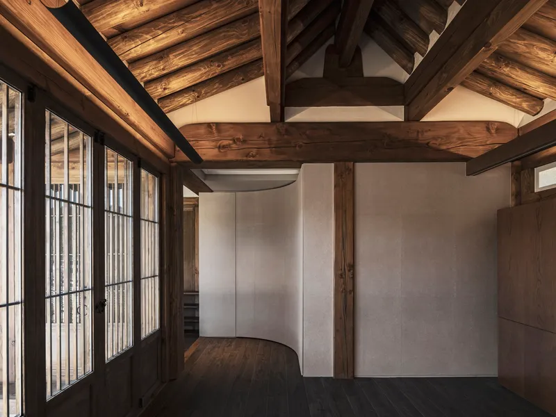 Curved partition walls beneath timber post-and-beam structure with paper screen doors at left