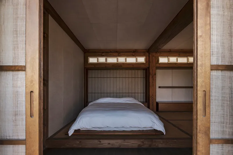Platform bed framed by timber posts with vertical slat screens and translucent sliding panels