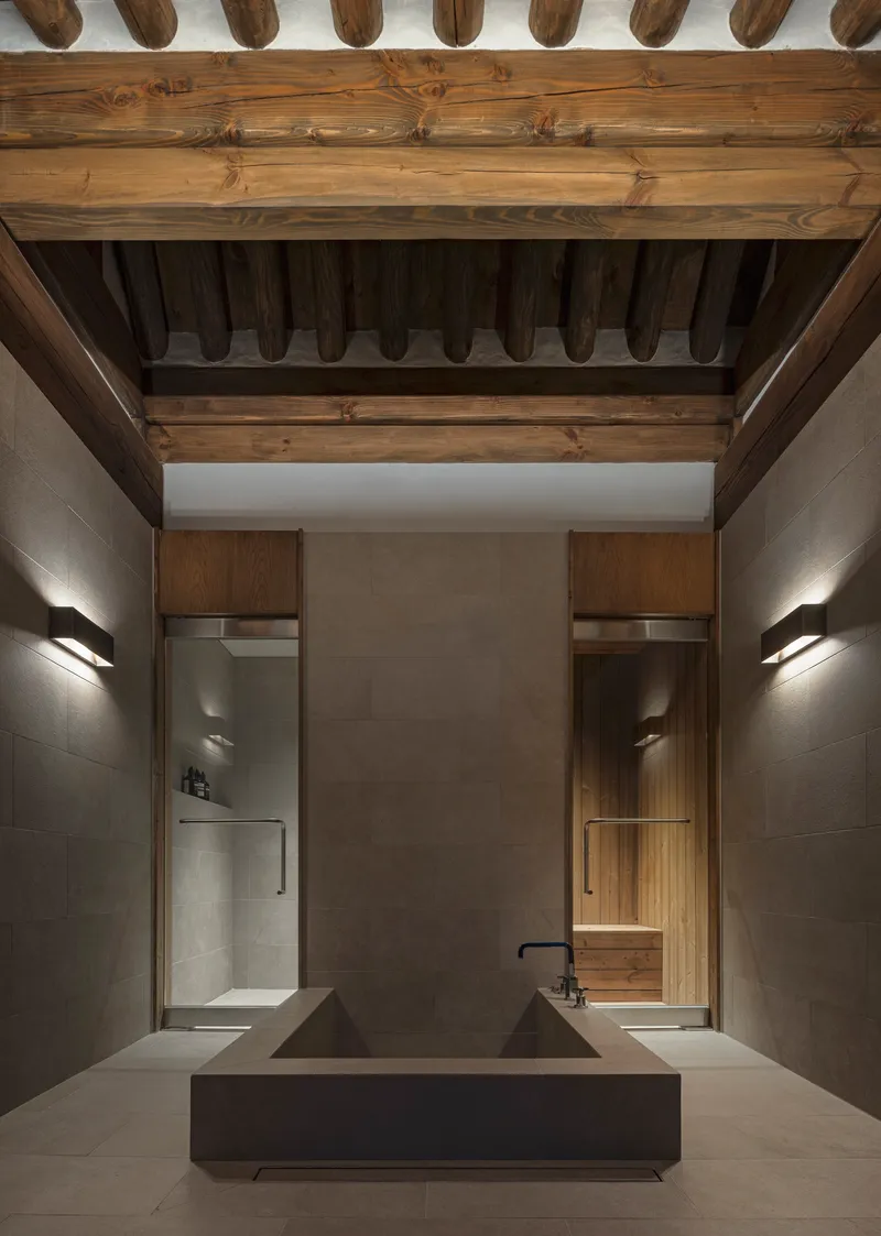 Bathroom with double concrete basin under exposed timber ceiling beams and flanking wall sconces