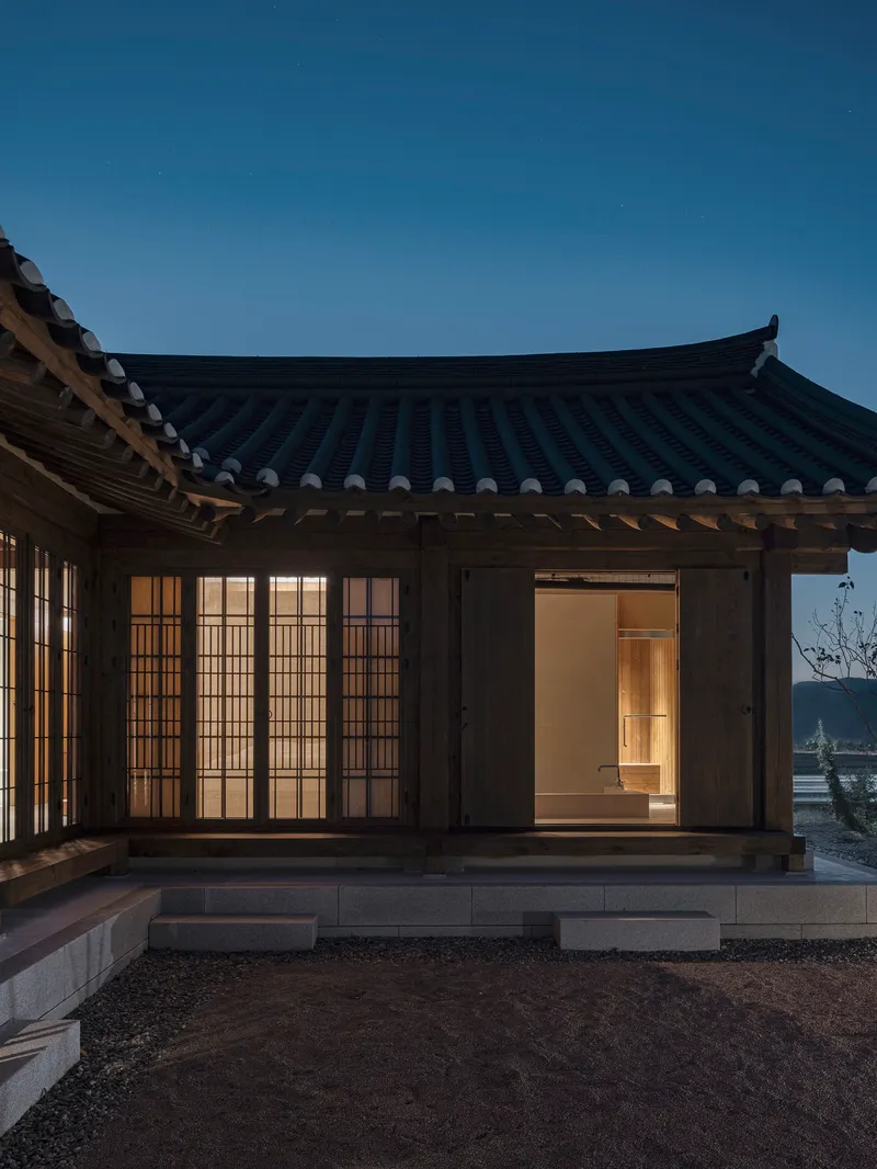 Timber pavilion with curved tiled roof and translucent gridded screens illuminated at dusk