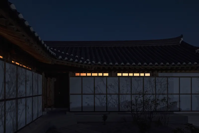 Courtyard facade with translucent panels and illuminated clerestory windows under sweeping tiled eaves at dusk