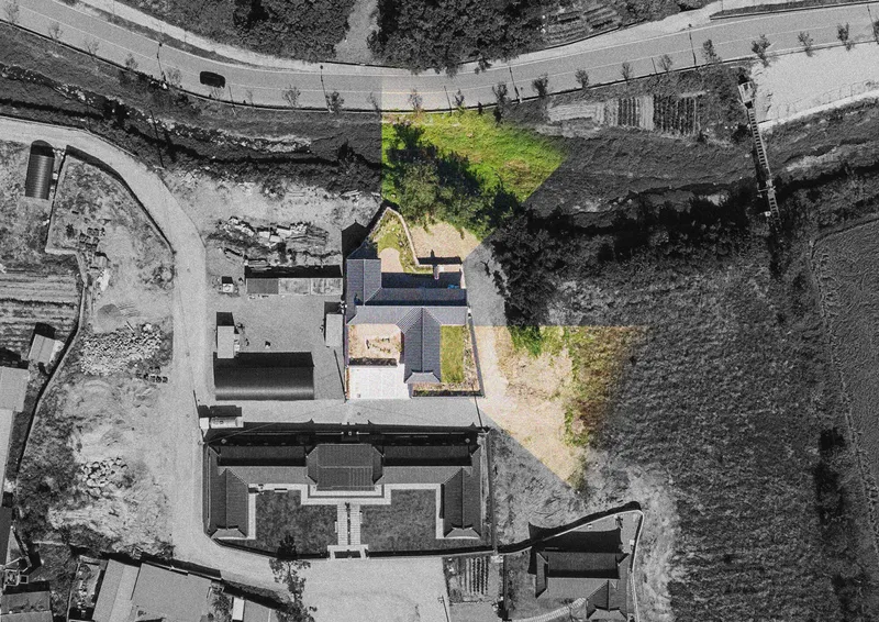 Aerial view of a cross-shaped compound with dark roofs and green courtyard spaces between surrounding agricultural fields