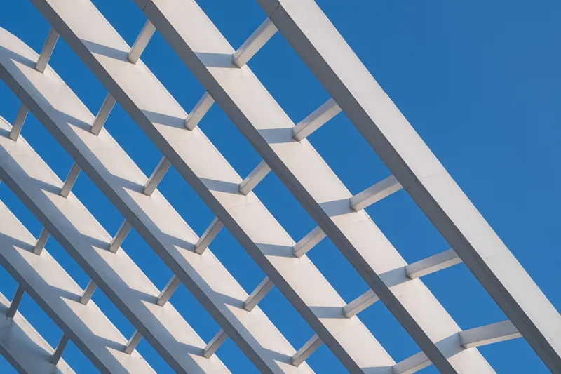Repeating white horizontal louvers casting sharp shadows against a deep blue sky
