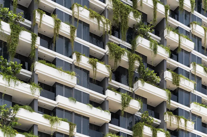 Residential tower facade with planted balconies and trailing greenery on white terraced slabs