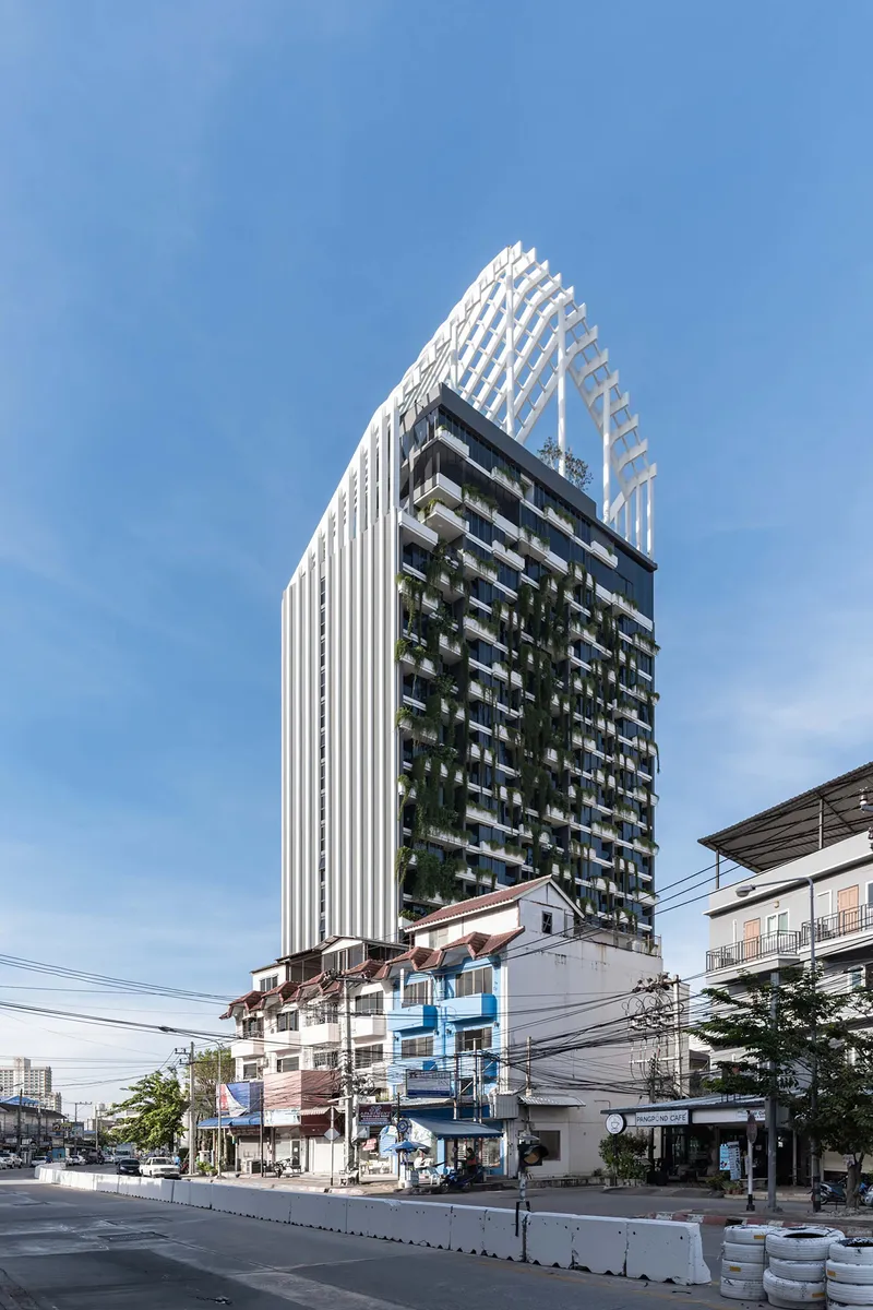 Street view of the high-rise tower with vertical white fins and planted balconies under a clear blue sky