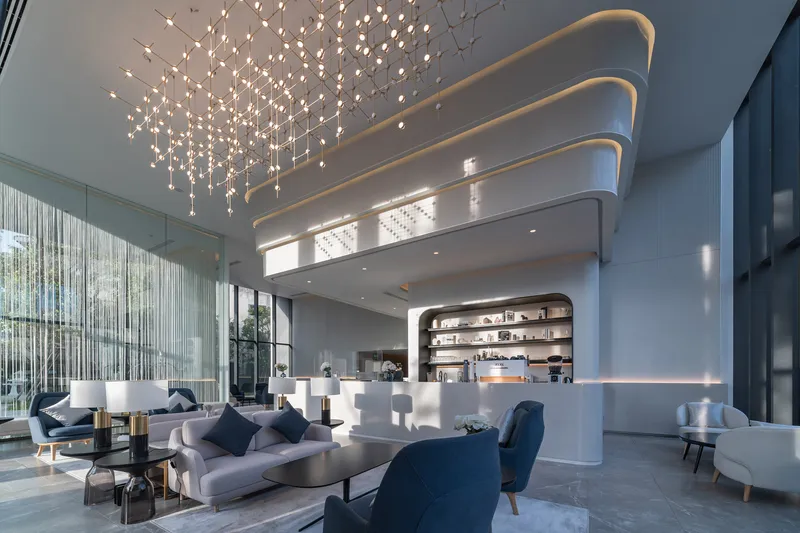 Double-height lobby with curved ceiling coves, cascading light installation, and curved reception desk below mezzanine