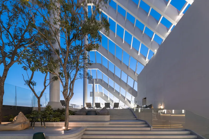 Outdoor terrace steps flanked by trees beneath the cantilevered tower facade at twilight