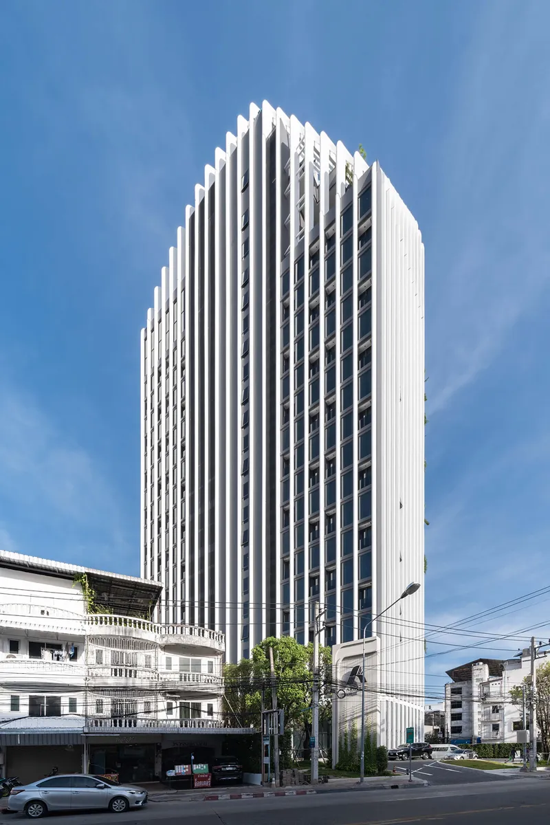 White vertical fin facade rising above low-rise neighbors and a street with a passing car