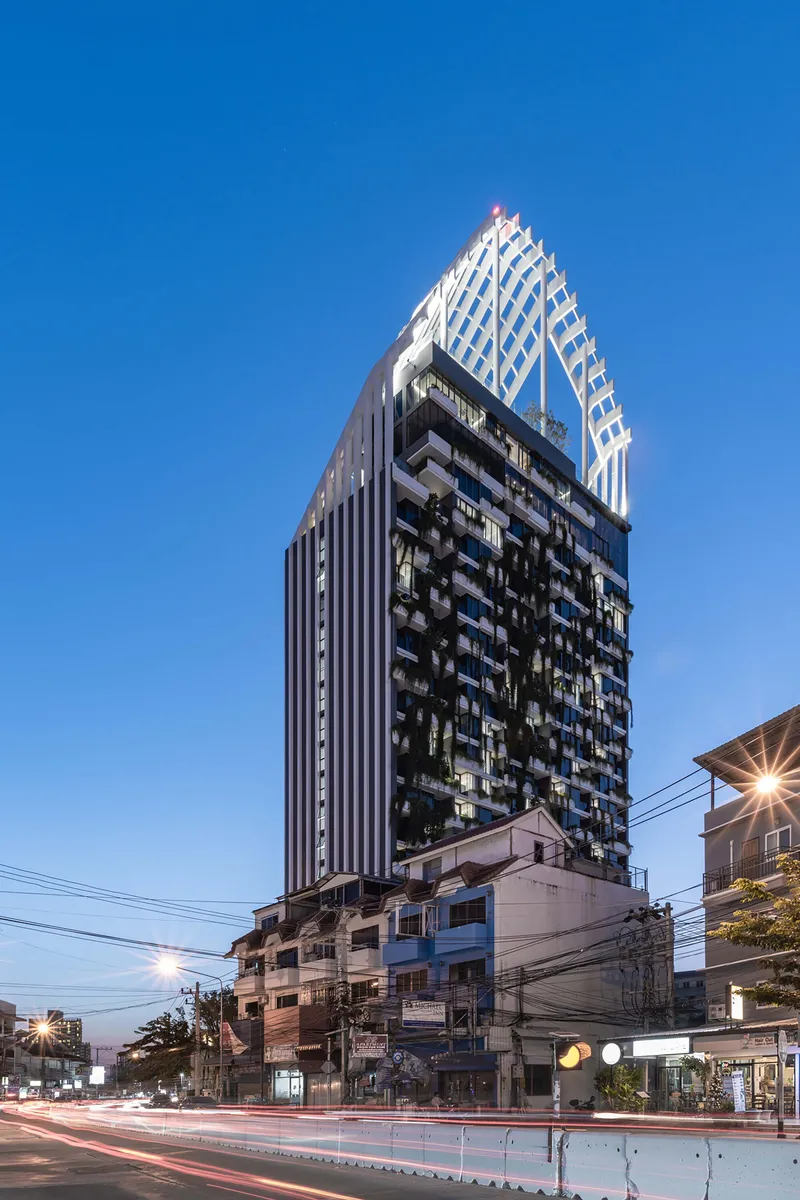 Street view at dusk with balconies, vertical fins, and light trails from passing traffic