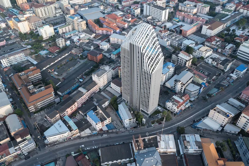Aerial view of the white-finned tower rising above a gridded urban neighborhood at dawn