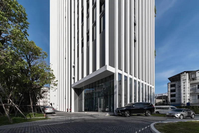 Ground-level corner showing the vertical louver facade above a glass-walled entrance with parked vehicles