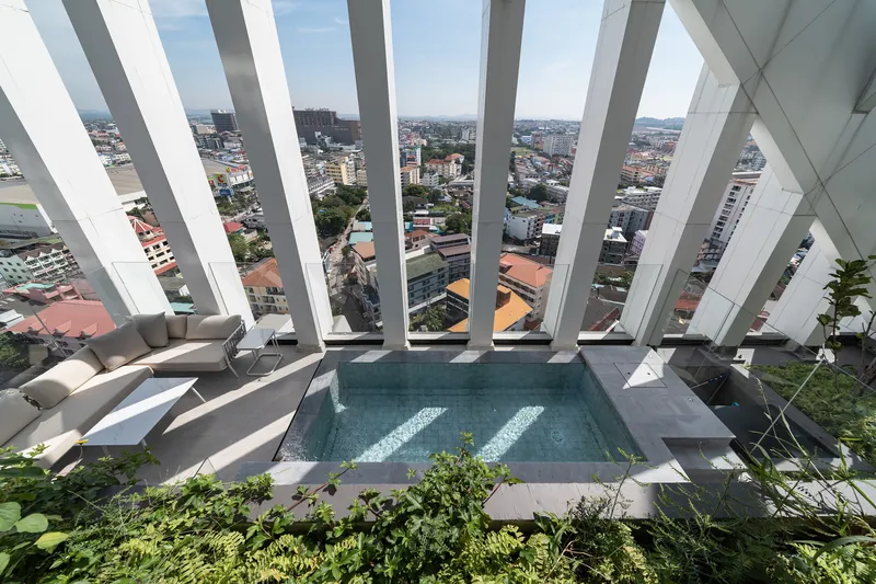 Rooftop pool terrace framed by angled white structural fins overlooking the low-rise cityscape
