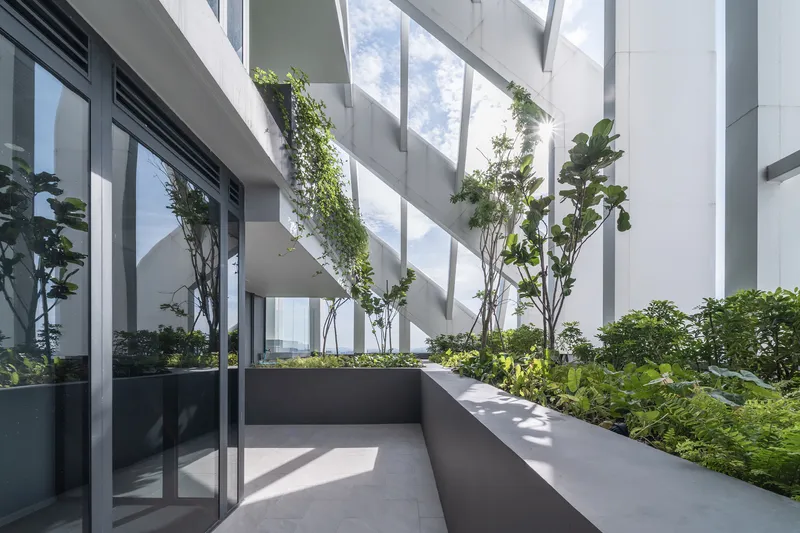 Planted terrace with raised grey planters and young trees beneath diagonal sunshading elements