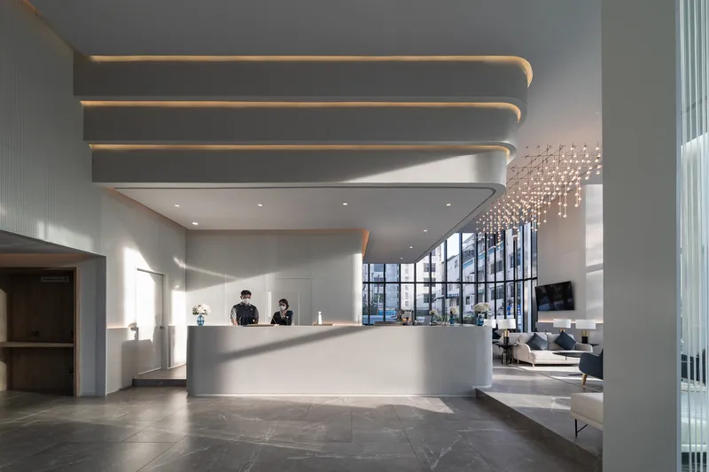 Double-height lobby with curved reception desk and layered ceiling coves with recessed lighting