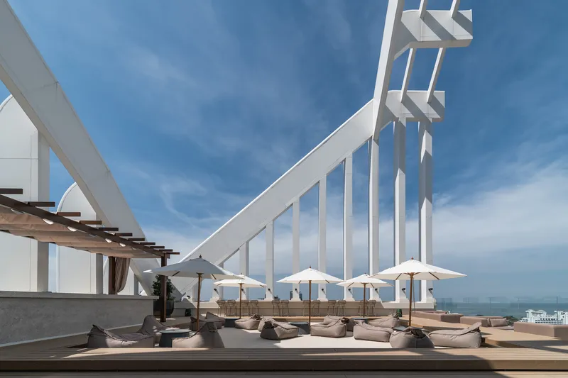 Rooftop lounge deck with white umbrellas and cushioned seating beneath angled white structural blades