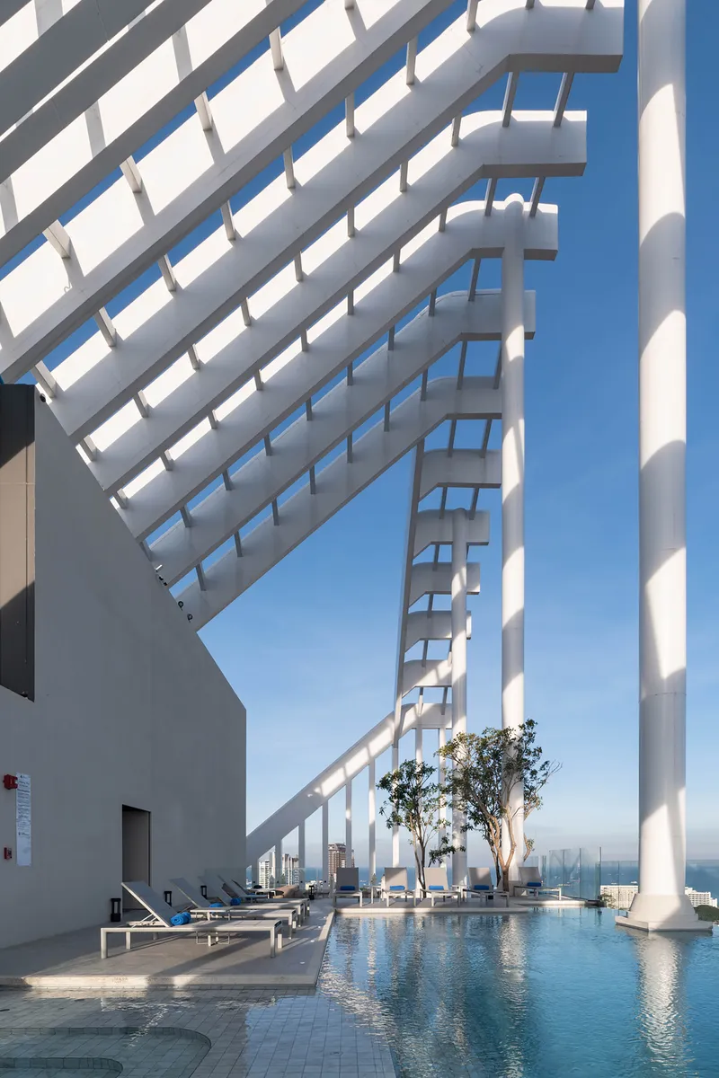 Rooftop pool framed by white diagonal louvers and cylindrical columns under clear blue sky