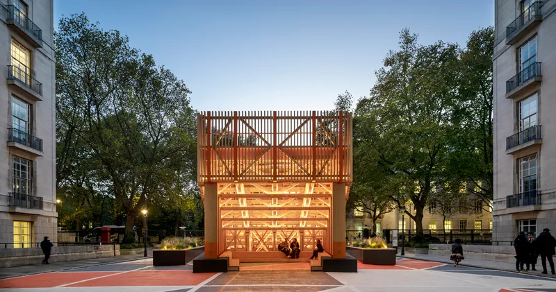 Front elevation of the illuminated timber structure set between trees at twilight
