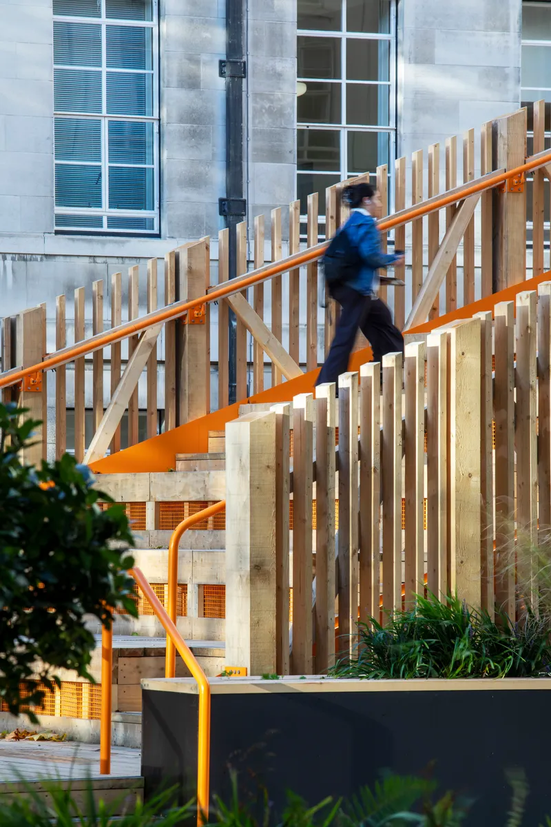 Person in motion ascending the staircase with vertical slatted timber balustrade and planted beds below