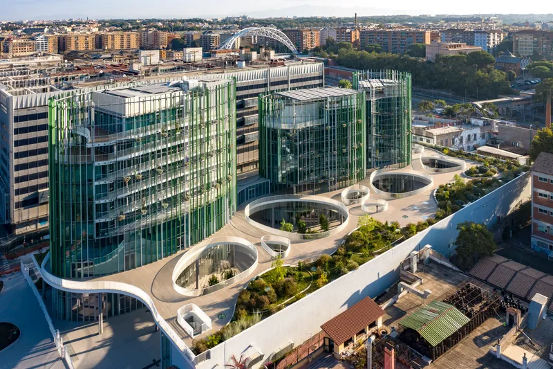 Aerial view of the undulating rooftop garden with circular planted voids and vertical glass fins in afternoon light