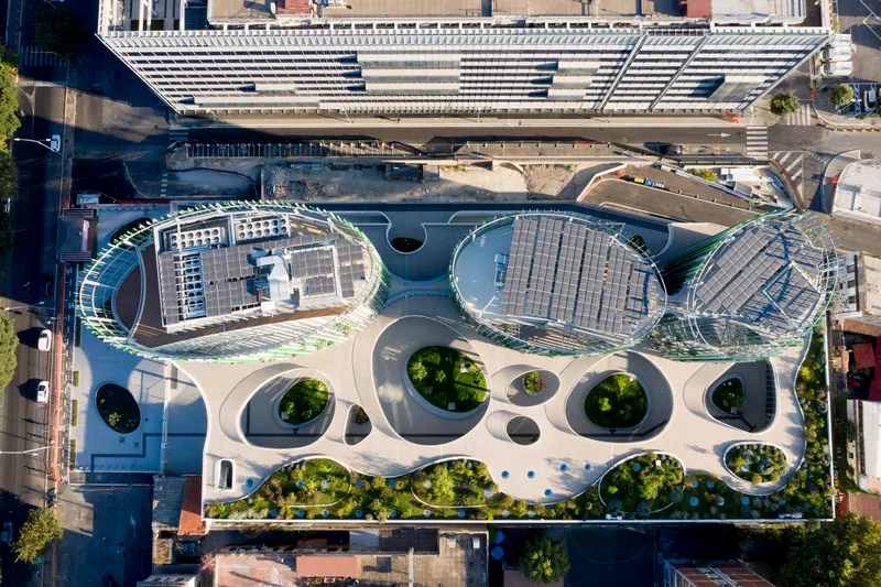 Aerial view of the curved roof plane with circular skylights and planted openings adjacent to striped canopy structure