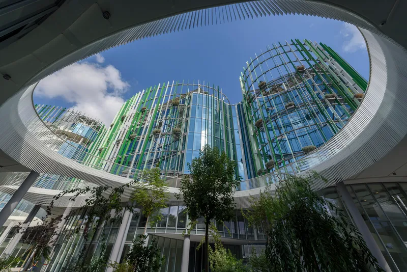 Upward view through circular courtyard opening framed by vertical louvres and planted trees below