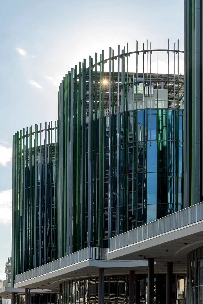 Facade detail of vertical green and blue louvres wrapping curved glass volumes at dusk