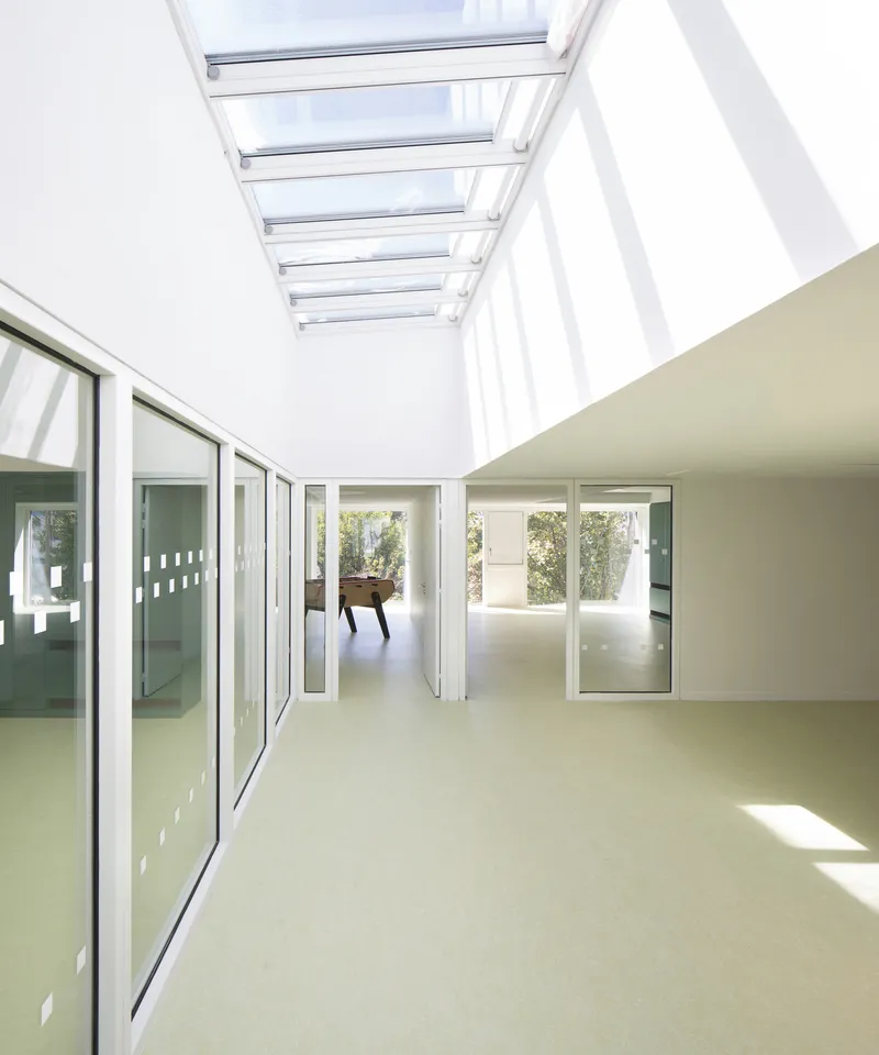 Skylit corridor with glazed walls connecting interior spaces with sunlight filtering through overhead louvers