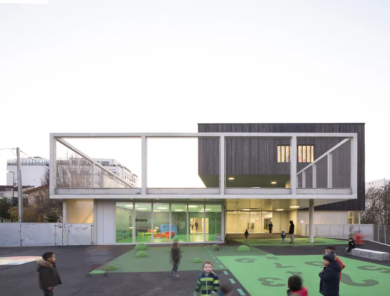 Two-storey facade with timber cladding above glazed ground floor and green play surface with children