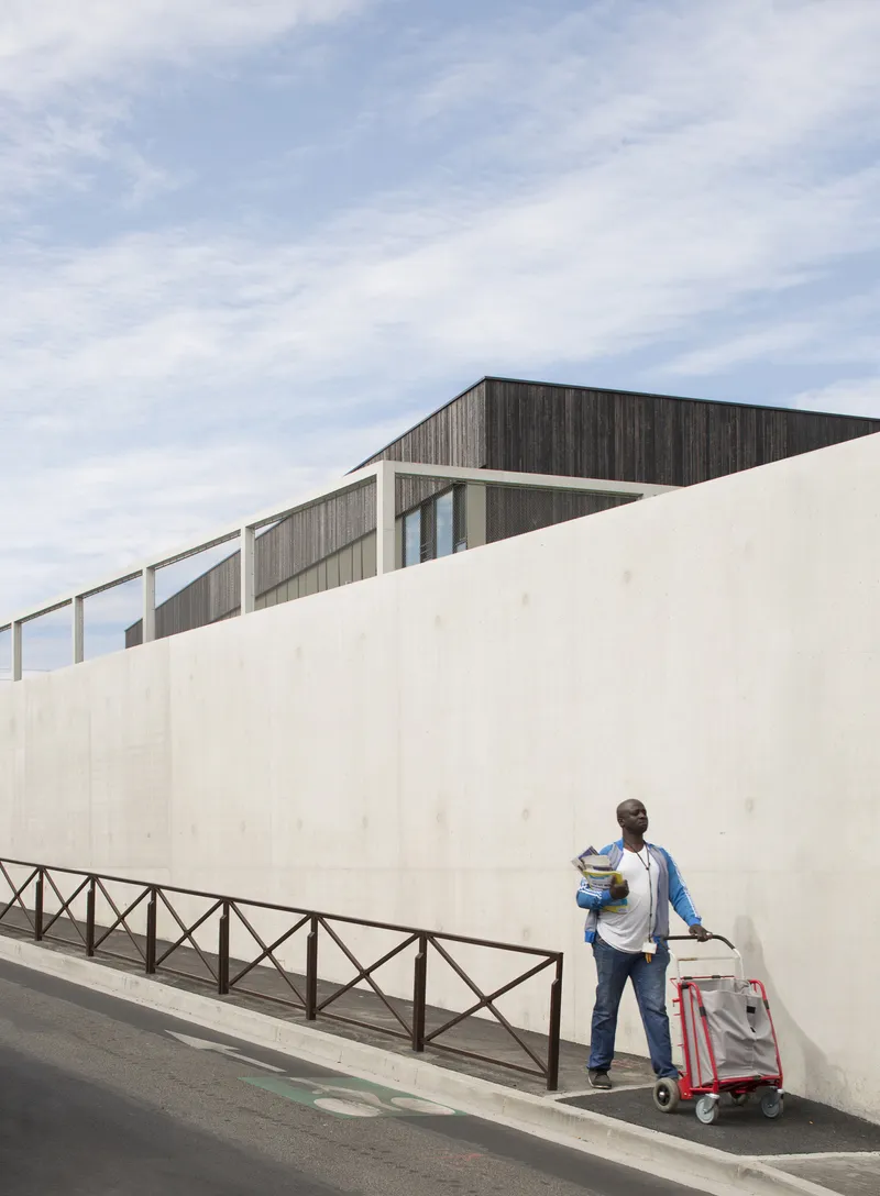 Delivery worker with cart passing along the street-level concrete wall below dark timber cladding