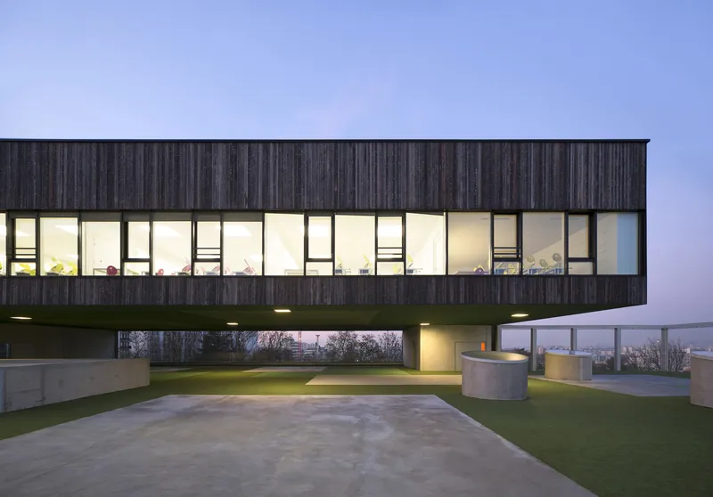 Elevated timber facade with illuminated interior corridor visible through glazing at dusk