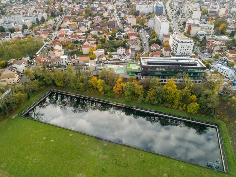 Aerial view of rectangular reflecting pool surrounded by lawn and autumn trees in residential district