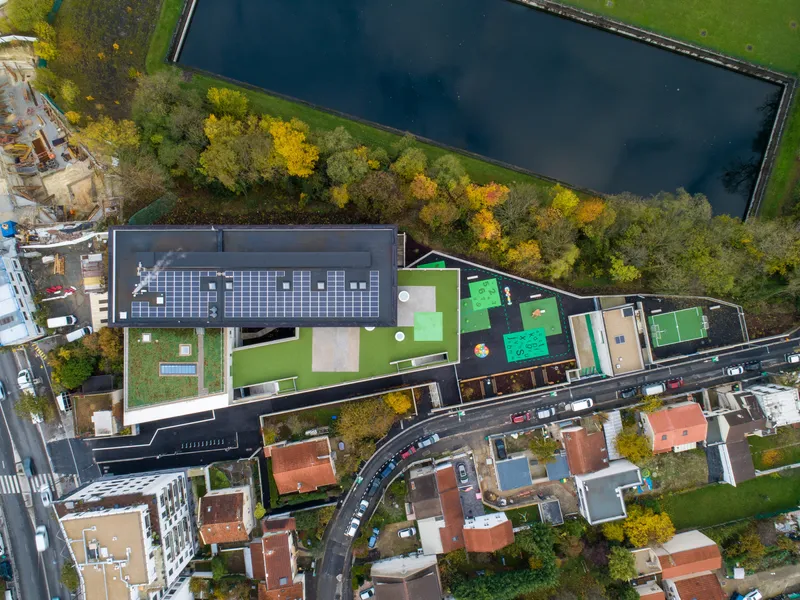 Drone view of rooftop with photovoltaic panels and green courtyard terraces beside dark reflecting pool