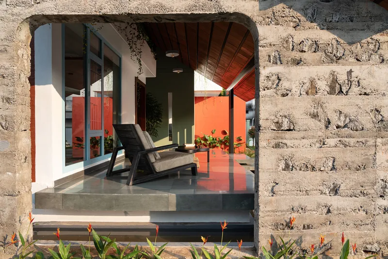 Arched opening in laterite wall framing seating area with polished concrete floor and bird-of-paradise plantings