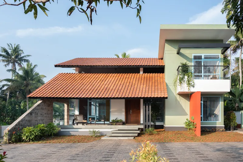 Two-story residence with red clay tile roof and pale green upper volume surrounded by coconut palms